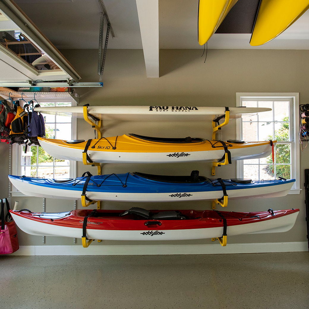 Stack of kayaks on a rack in a garage with visible brand names.