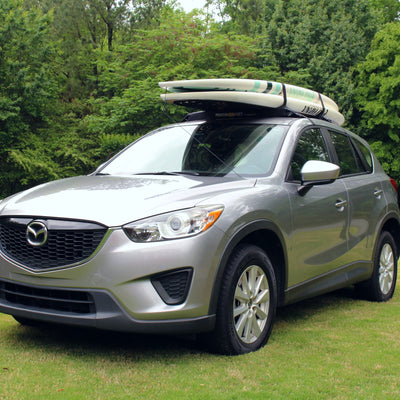 Silver Mazda CX-5 with a surfboard on top parked on grass