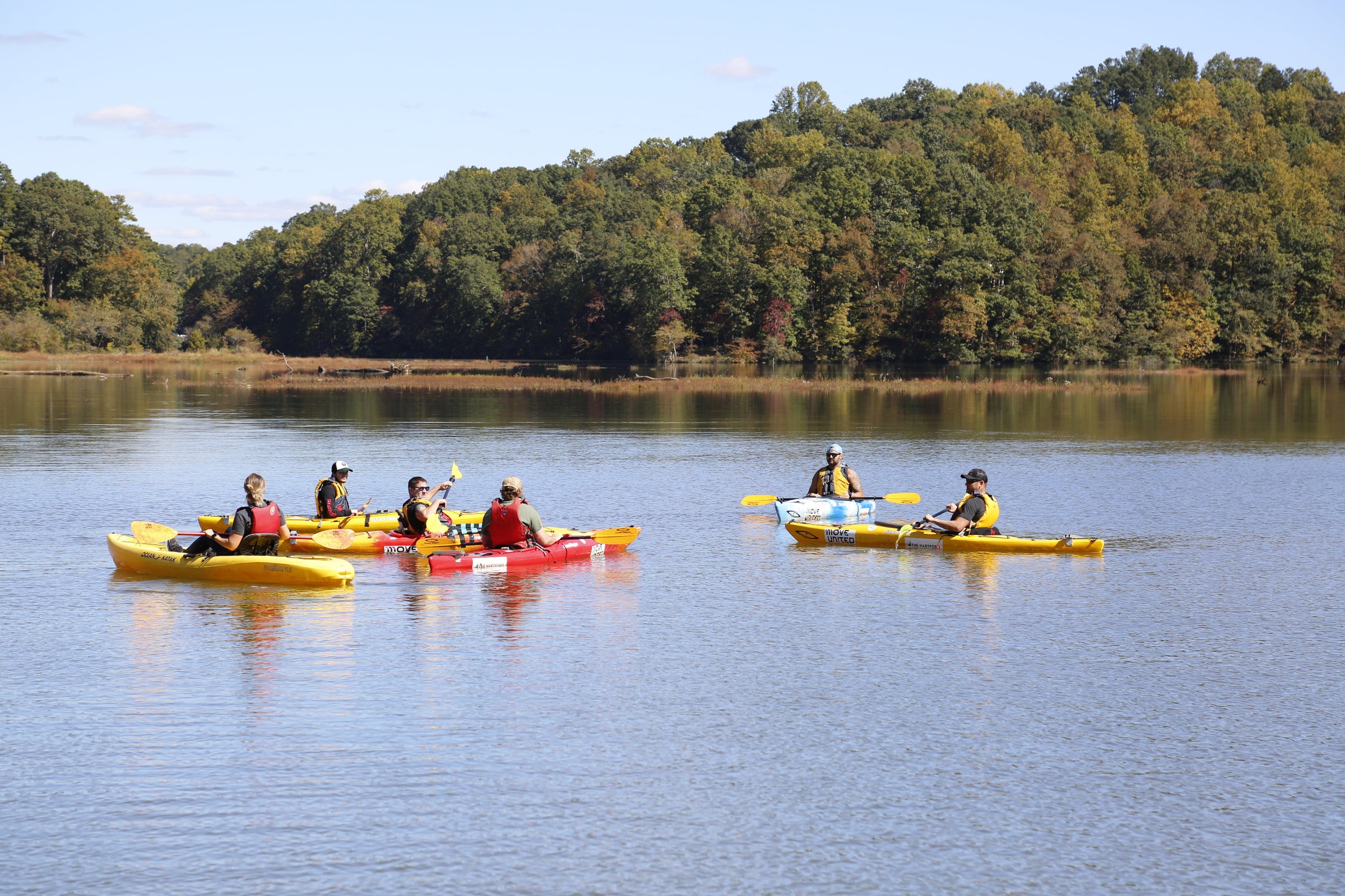 People kayaking on a calm lake with trees in the background