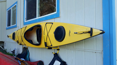 One kayak, one paddle, and one life jacket resting on a folding kayak rack on a wall outside