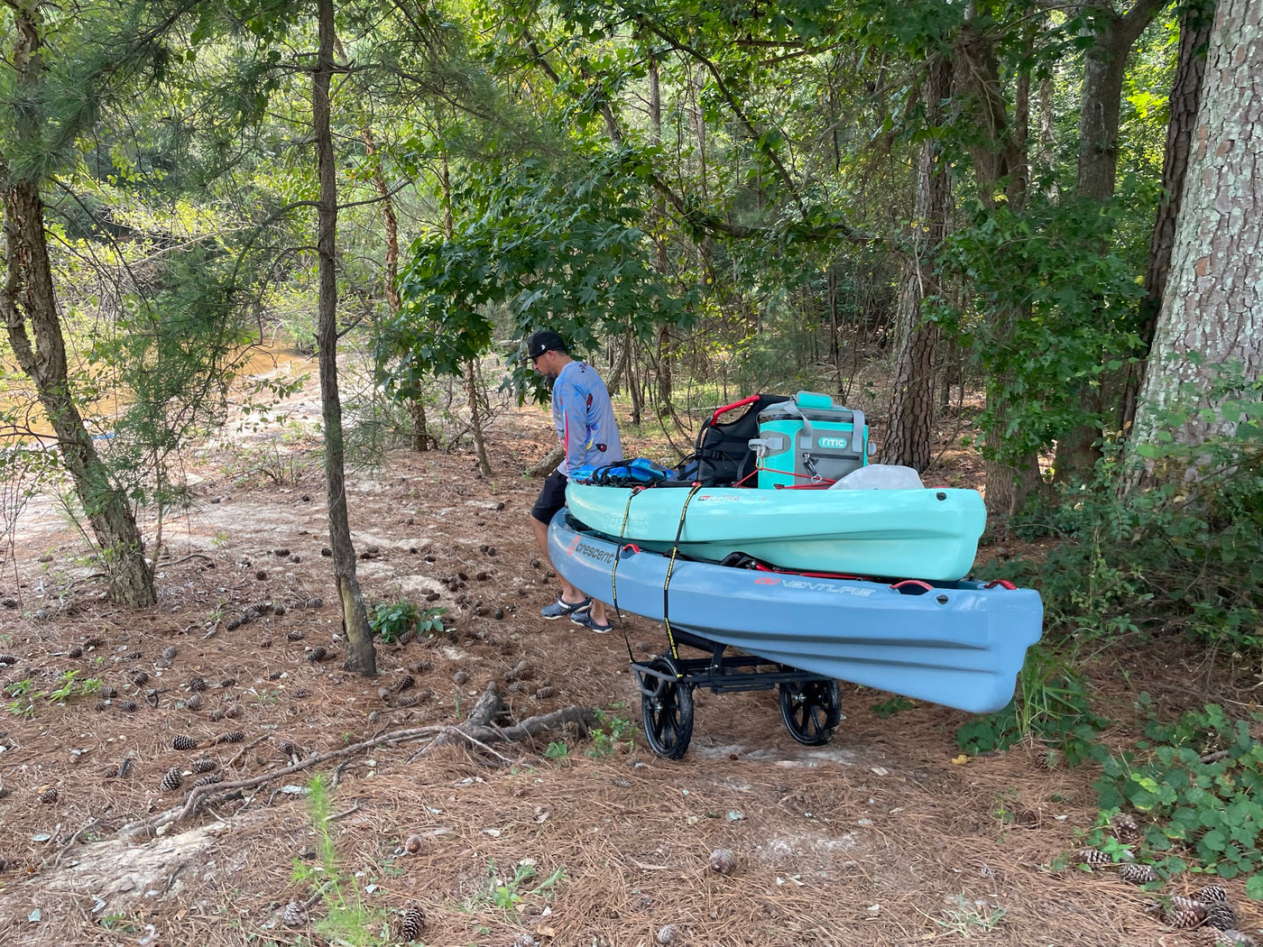 Man pulling 2 kayaks on the all-terrain cart through the woods